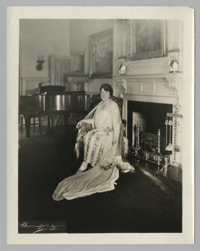 Mary Roberts Rinehart portrait in white flowered dress, seated by fireplace